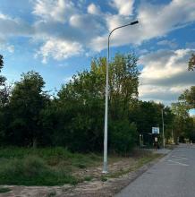 Na zdjęciu widać nowo zamontowaną latarnię uliczną przy ul. Literatów. Słup z oprawą LED stoi przy jezdni w pobliżu przystanku autobusowego, a w tle znajdują się drzewa i chodnik. Nowe oświetlenie poprawia bezpieczeństwo i widoczność po zmroku.