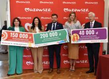 Cztery osoby trzymających w rękach symboliczne czeki z kwotami dofinansowania.