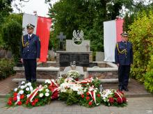 Dwóch strażników miejskich pełni wartę przy nagrobku na cmentarzu.