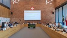 Grupa osób siedzi za stołami na sali posiedzeń