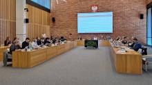 Sala obrad Rady Miejskiej Konstancin-Jeziorna podczas sesji. Radni siedzą przy stołach i uczestniczą w posiedzeniu.