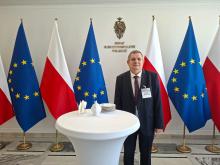 zdjęcie Wojciecha Guszkowskiego na tle flag Polski i UE