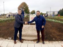 Burmistrzowie Michał Wiśniewski i Fabian Nitz ściskają dłonie na nowym rondzie w Denzlingen, przed kamiennym herbem Konstancina-Jeziorny. W tle tablica partnerska i uczestnicy uroczystości.