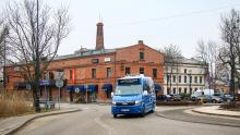 Niebieski autobus linii L21 jedzie ulicą na tle zabytkowego, ceglanego budynku w centrum miasta.