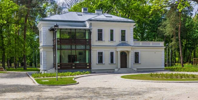 Widok na odrestaurowany budynek willi Kamilin od ulicy Piłsudskiego, na planie litery L z ozdobną drewnianą werandą. Tło stanowią wysokie drzewa . 