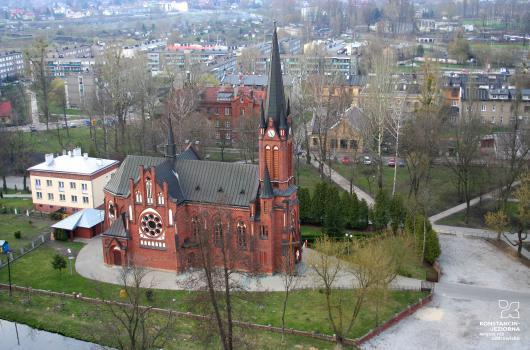 Duży budynek kościoła z czerwonej cegły, dach ciemny, widoczny z boku z lotu ptaka, z tyłu widoczne inne budynki