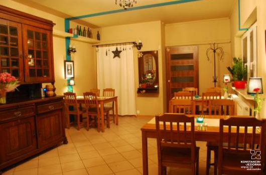 Wnetrze restauracji, po lewej stronie ozdobny kredens drewniany, w sali stoliki i krzesła drewniane, po prawej stronie okno