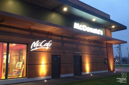 Duzy budynek podświetlony od dołu, z neonem McDonalds u góry oraz neonem McCaffe na ścianie na dole, ściany obłożone sidingiem drewnianym, po prwawej widoczne dużo okno