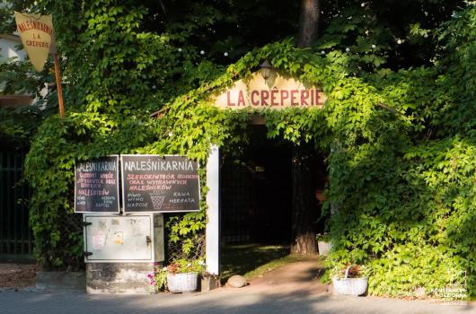 Wejście z szyldem, zarosniete bluszczem, obok tablica z nazwą i wypisanym menu