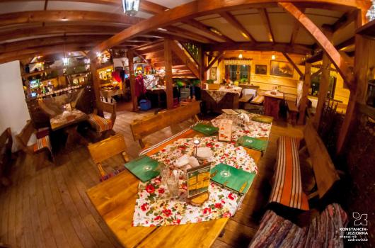 Wnetrze restauracji w stylu rustykalnym drewniane długie stoły, drewniane ławy, strop z drewnianymi9 belkami, na ścianach deski, 
