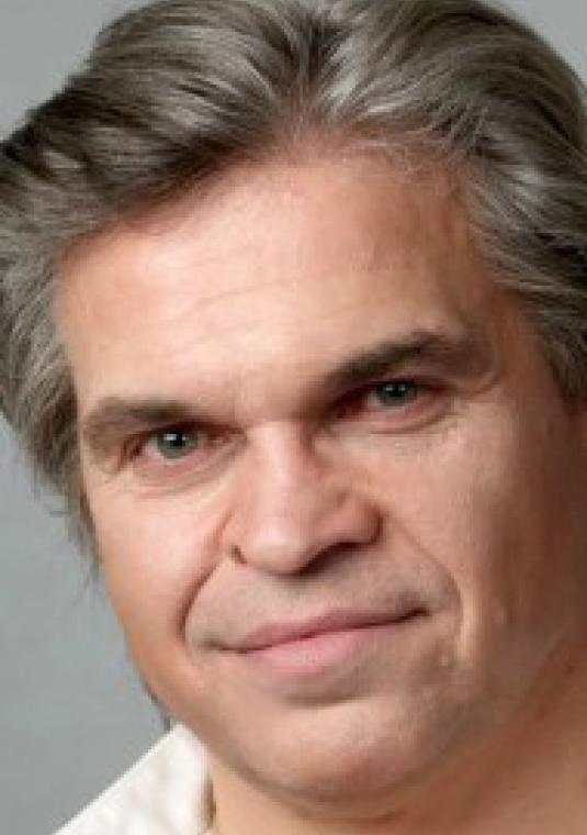 Portret. Mężczyna w średnim wieku. Ubrany w białą koszulę. Siwe włosy średniej długości.