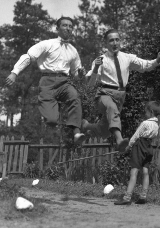 Czarno-białe zdjęcie, dwóch mężczyzn skacze w biegu, w tle dziecko.