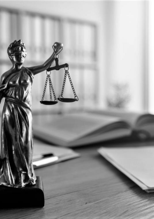 Czarno-białe zdjęcie. Na biurku stoi figurka kobiety z zasłoniętymi oczami w lewej ręce trzyma wagę a w prawej miecz.