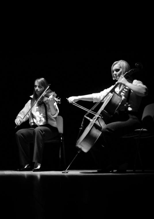 Biało-czarne zdjęcie czterech osób ze skrzypcami w rękach. Jedna z nich ma wiolączelę. są to trzy kobiety i jeden mężczyzna. Siedzą na krzesłach w półkolu.