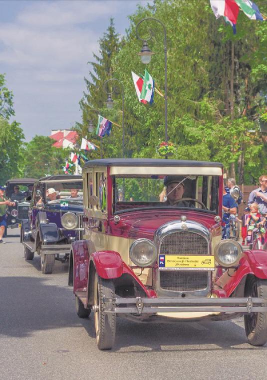 Zdjęcie starych samochodów na ulicy. Na chodniku stoja ludzie.