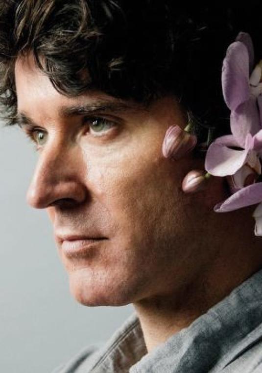 Profil młodego mężczyzny, który za ucho ma włożone kwiaty orchidei.