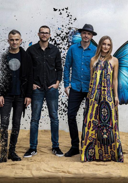 na szarym tle stoi kobieta w kolorowej sukience obok trzech mężczyzn