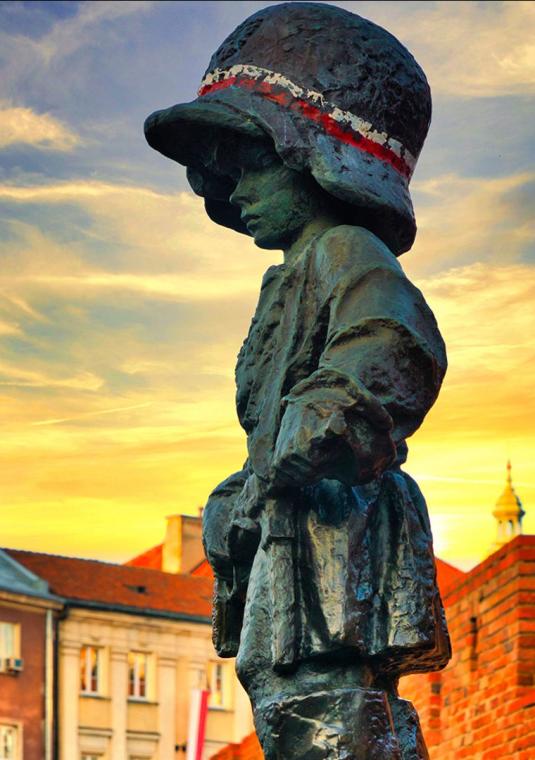Pomknik warszawskiego powstańca na tle zachodu słońca i kamieniczek.