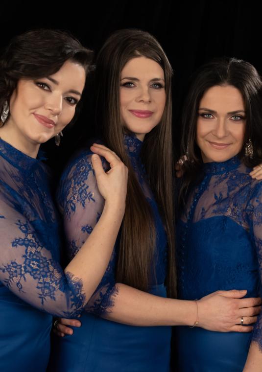 Zdjęcie czterech kobiet w eleganckich, niebieskich sukniach na czarnym tle.