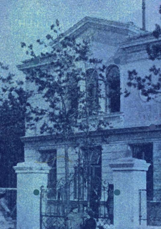 Archiwalna fotografia zabytkowej, piętrowej willi w Konstancinie, utrzymana w monochromatycznej, niebieskiej tonacji. Budynek o klasycznej architekturze z ozdobnymi gzymsami jest otoczony drzewami i ozdobnym ogrodzeniem z murowanymi słupkami na pierwszym planie.