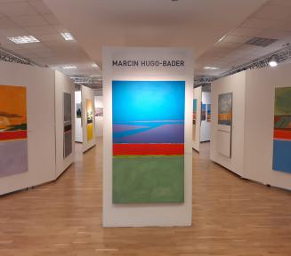 Sala wystawiennicza. Na ścianach znajdują się kolorowe, abstrakcyjne obrazy namalowane przez Marcina Hugo-Badera.