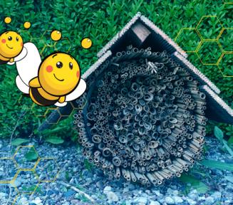 Na trawniku stoi domek dla owadów wykonany z drewnianych patyków. Nad nim rysunki dwóch pszczół.