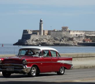 Stary zabytkowy czerwony samochód jedzie ulicom. W tle widać morze. 