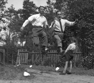 Czarno-białe zdjęcie, dwóch mężczyzn skacze w biegu, w tle dziecko.