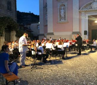 Grafika przestawia orkiestrę grającą koncert na tle katedry.