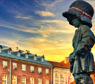 Pomknik warszawskiego powstańca na tle zachodu słońca i kamieniczek.