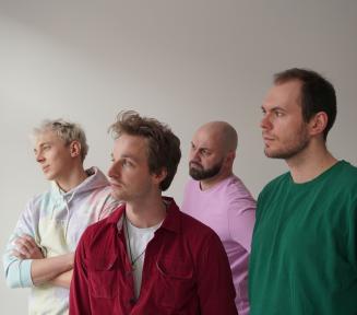 czterech mężczyzn w kolorowych bluzach na tle beżowej ściany - patrzą w lewą stronę