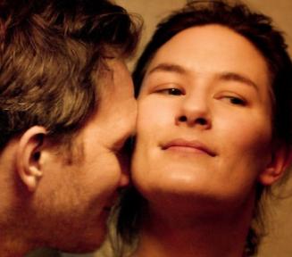 kadr z filmu Być kochaną - duże zbliżenie na twarze kobiety i mężczyzny, ciepłe odcienie, uśmiechnięci, intymny moment przytulenia